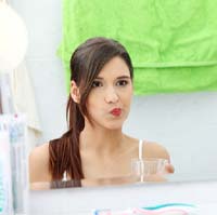 Woman rinsing with mouthwash in front of mirror
