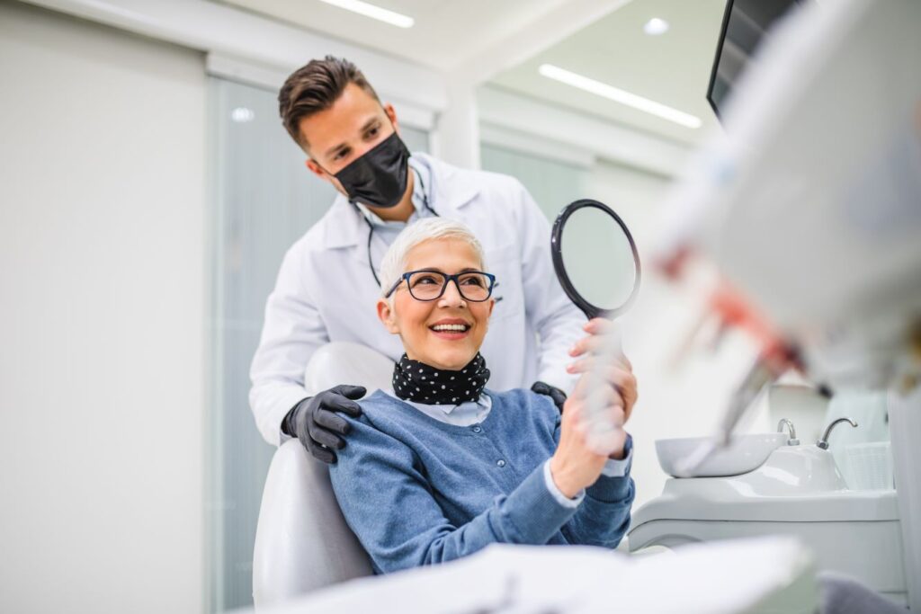 A woman looking in the mirror at her dental implants at her dentist's office